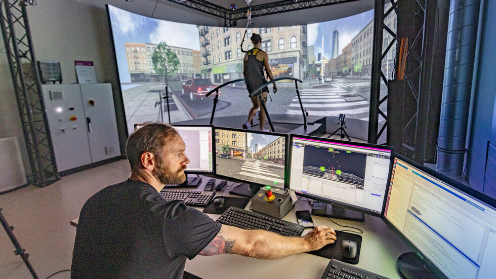 Das Ganganalyse-Labor (GRAIL) der TU Chemnitz ermöglicht Grundlagen- und Anwendungsforschung innerhalb einer interaktiven Echtzeit-Virtual-Reality-Umgebung. Die virtuelle Welt wird auf einen 240 Grad „curved Screen“ projiziert. Damit die Probandin während der Ganganalyse auf dem Laufband nicht stürzt, ist sie mit einem Gurt gesichert. Das Ganganalyse-Labor (GRAIL) der TU Chemnitz ermöglicht Grundlagen- und Anwendungsforschung innerhalb einer interaktiven Echtzeit-Virtual-Reality-Umgebung. Die virtuelle Welt wird auf einen 240 Grad „curved Screen“ projiziert. Damit die Probandin während der Ganganalyse auf dem Laufband nicht stürzt, ist sie mit einem Gurt gesichert.